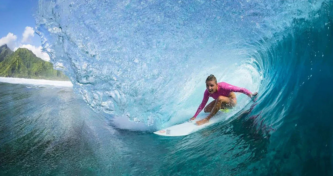 Surfer riding a powerful barrel wave at Teahupo'o with lush mountains in the background.