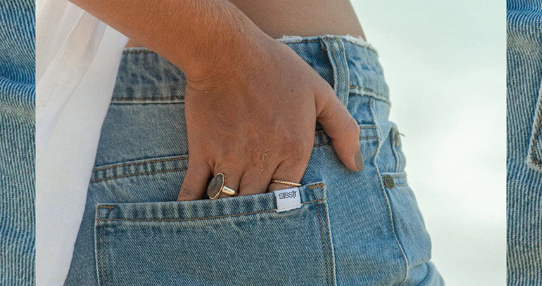 Close-up of a hand with rings tucked into the back pocket of light blue denim jeans.