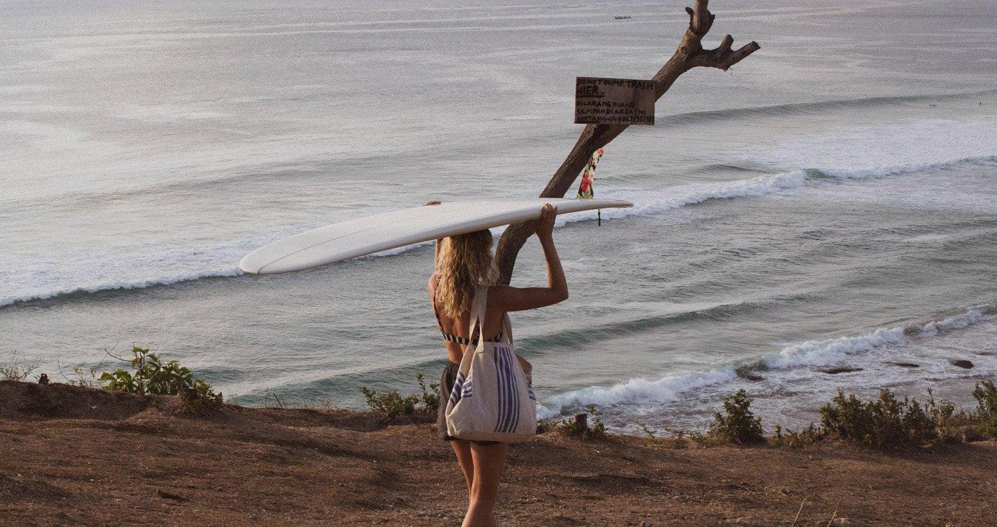 Surfer carrying a board, overlooking serene ocean waves in an autumn setting.