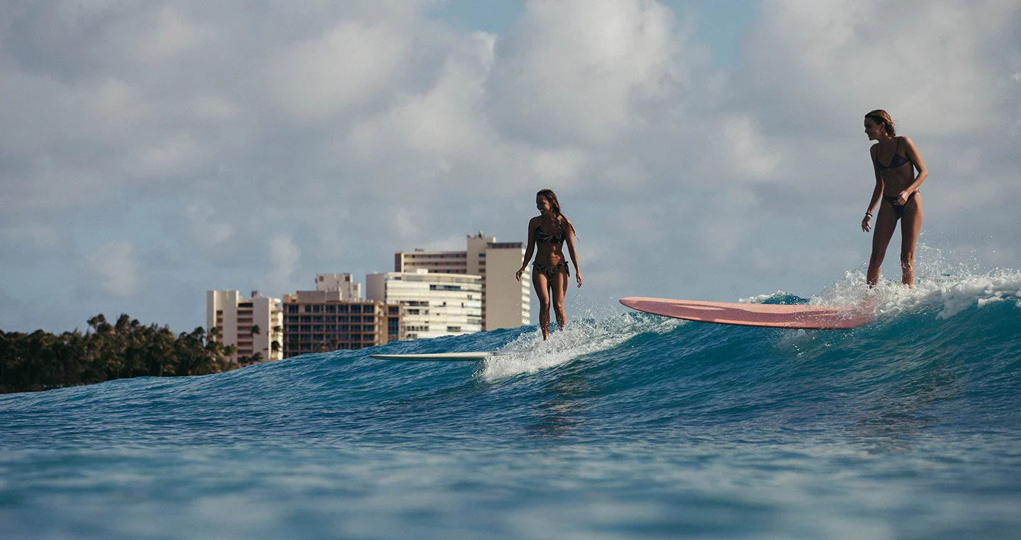 Two women surfing Waikiki waves with city skyline in the background.