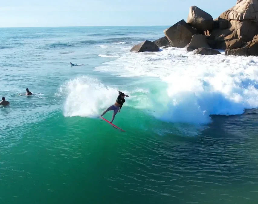 Surfer riding a vibrant turquoise wave near rocky shoreline in Mexico.