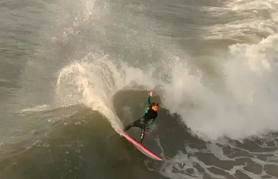 Surfer carving through a powerful wave on a pink surfboard in California.